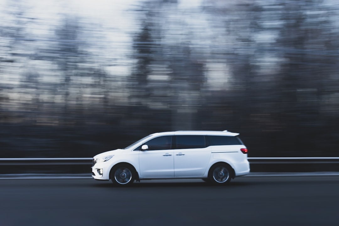 A white car driving down a road next to a forest